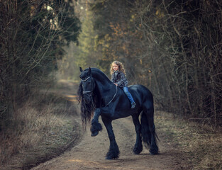 Beautiful girl sitting on black Frisian horse  in spring in the forest