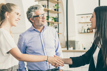 Obraz premium Happy confident female manager meeting with customers and shaking hands. Man and women in co-working space. Side view. Partnership or business meeting concept