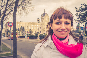 Young girl traveler with white jacket and red scarf looking at camera and smile, Kunsthistorisches Museum of Art History or Fine Arts in Vienna city historical centre background, close-up view