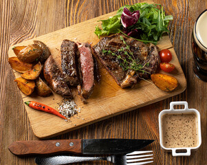 Beef steak served with vegetables and baked potatoes on wooden board with sauce on wooden table top view. High quality photo