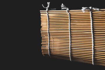 Thin bamboo sticks are tied with a rope. Wooden mat for making sushi and rolls. Japanese cuisine chef's tool on a dark background.