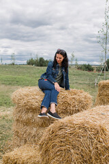 Naklejka na ściany i meble girl on sheaves of hay in summer with dark hair beautiful