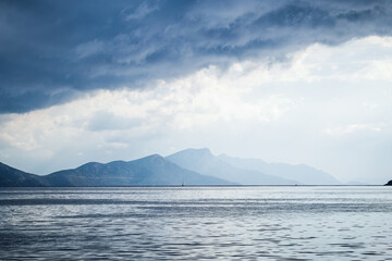 Dark clouds in the open sea. On the horizon are mountains on an island. - 412921430