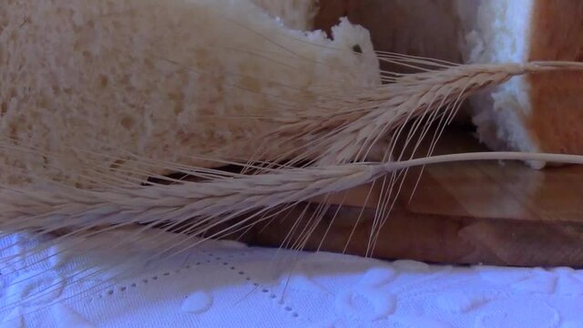 Close up on a appetizing slice of homemade bread decorated with dry wheat ears on a white embroidered tablecloth. 