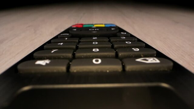 Black TV remote control with coloured buttons and display lies on brown wooden table extreme closeup. Concept multimedia controller