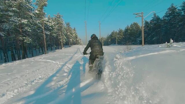 Cyclist in Black Clothes, Helmet and Snow Glasses Riding on Electric Bike in the Snow in Winter Forest. E-Bike Riding and Drifting at Cold Sunny Day - Super Slow Motion