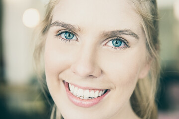 Face of happy beautiful young blonde woman with blue eyes and white teeth looking at camera and smiling. Closeuo shot, front view. People or beauty care concept