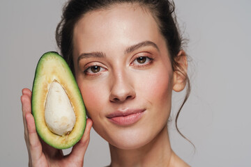 Pleased half-naked woman looking at camera while posing with avocado
