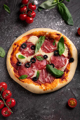 Flat lay of freshly baked pizza with olives and basil on a black background