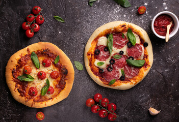 Two pizzas with tomatoes and basil on black table