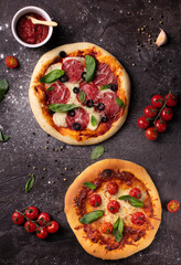 Two pizzas with tomatoes and basil on black table