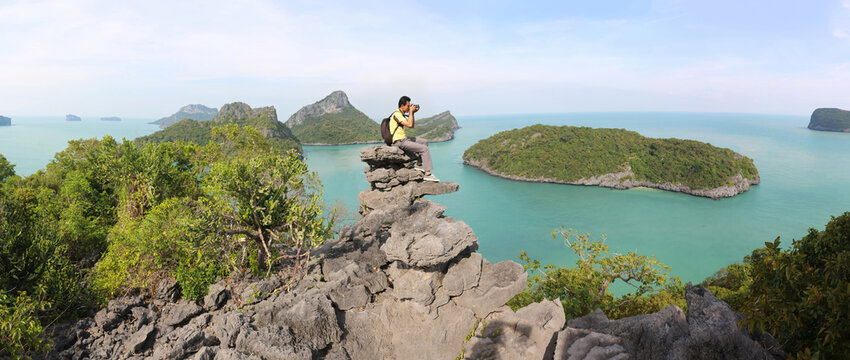 Asian tourists sitting and using a camera on top of a limestone mountain in Ang Thong Marine National Park.