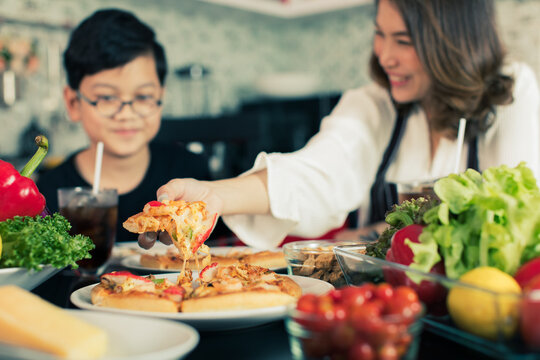 Asian Mom And Son Sitting In Home Kitchen And Eating Homemade Pizza Together With Various Kinds Of Vegetables. Idea For Happiness Of Good Time Sharing In Family