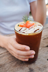 Woman held a glass of strawberry syrup and espresso shot in a glass on the table.