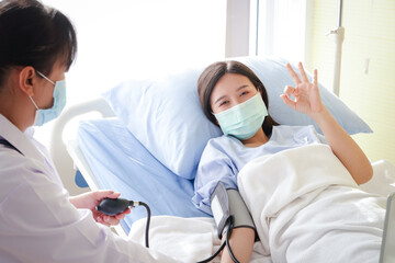 Asian female patients Wear a blue mask and lie on a hospital bed. Raise your hand. Okay. The doctor measures the patient's pressure. Concept of medical service, health insurance