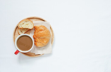 Hot coffee cup beside fresh croissant on wooden tray placed on white tablecloths