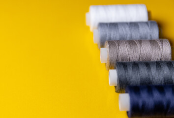 spools of colored thread lie in a row on a yellow background. Selective focus