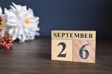September 26, Date cover design with calendar cube and white Paeonia flower on wooden table and blue background.