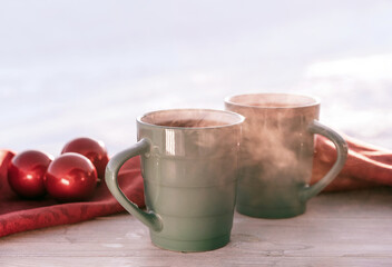 Vintage rustic card with green porcelain cups of tea on white wooden table decorated with red Christmas balls. Winter seasonal holiday background. Food and drink concept. Closeup.