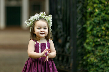 Beautiful two year old girl with a flower floral crown and a purple dress outside near an iron gate