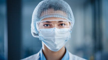 Close Up Portrait of a Beautiful Female Doctor or Surgeon Wearing a Protective Face Mask, Goggles and Disposable Surgical Cap. Laboratory Scientist Calmly Looking at Camera. Covid-19 Pandemic Concept.