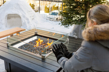 Woman sitting with a coat in winter in front of an outdoor fireplace