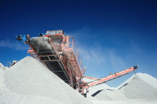 Working mobile crusher machine on the background of crushed stone hills and blue sky, close-up.