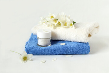 Obraz na płótnie Canvas Terry towels with body care cream, delicate white flowers on a white background, side view
