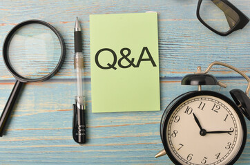 Top view of a magnifying, pen, alarm clock and spectacles with text Q&A on wooden background.Selective focus.