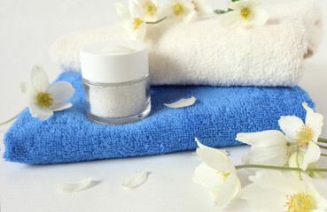 Obraz na płótnie Canvas Terry towels with body care cream, delicate white flowers on a white background, close-up