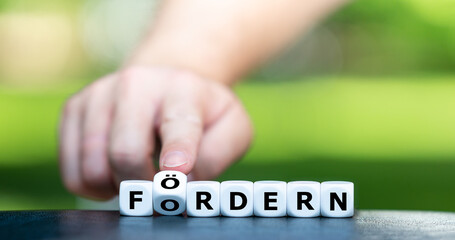 Fordern und fördern. Hand dreht Würfel und ändert den Ausdruck 