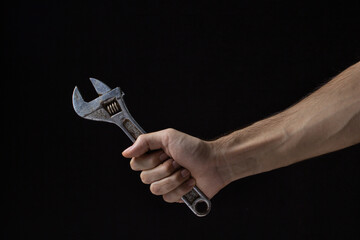 Adjustable wrench on a black background. Old work tool. A man's hand holds an adjustable wrench.