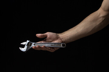 Adjustable wrench on a black background. Old work tool. A man's hand holds an adjustable wrench.