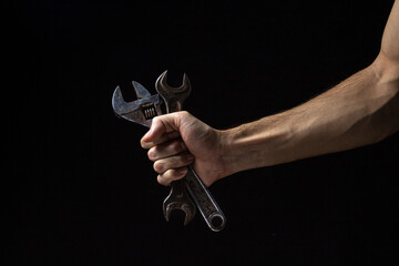 Wrench and adjustable wrench on a black background. Old work tool. A male hand holds a spanner and an adjustable wrench.