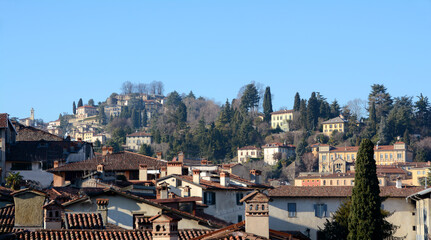 Fototapeta na wymiar Roofs and chimneys in the residential area of Bergamo Alta with hills and elegant villas in a typical and picturesque scenery of Italy. 