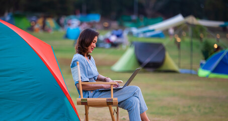 Female traveler sitting beside camping tent and using notebook laptop computer working with other...