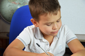 A child of primary school age do homework. The boy does his homework at his desk at home. The student pupil has been bored on the lesson. Back to school. Lovely first grader.