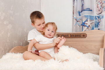Older brother tickles younger sister's bare feet on bed at home