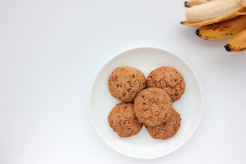 Oatmeal banana cookies on white table. Overhead view of oat biscuits and yellow fruits on white background with copy space