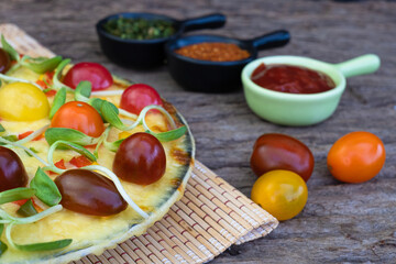 Close up homemade veggie pizza with cherry tomatoes and other ingredients on a wooden background