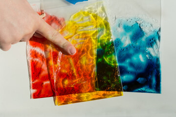 Plastic baggies of colored gel used to learn about primary colors, color mixing, and sensory play; child's hand touches bag with pointer finger