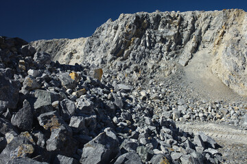 Steep cliffs and stone scree in a quarry against the background of a  dark blue sky.