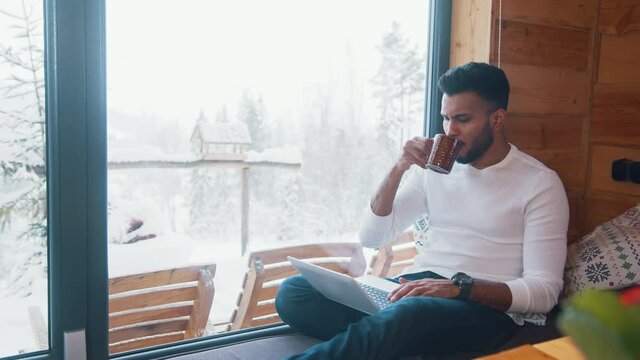 Young indian man drinking coffee and working on laptop on winter day. High quality 4k footage