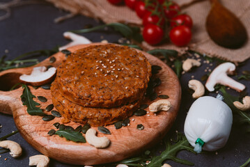 raw vegan burger close up on black background with vegan cheese and arugula leaves on hessian fabric. shiitake mushrooms, cherry tomatoes, sesame seeds all around with cashew nuts. copy space