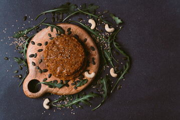 vegan burger top view on black background with pumpkin seeds, arugula leaves, cashew nuts and sesame seeds. inviting nutritious legumes hamburger