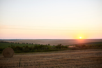 Sunset over natural field landscape in summer with light blue sky. Stubble field with straw bale....