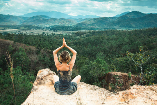 Young yoga woman meditates on a cliff top in a canyon.
