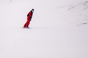 A guy in a red jumpsuit eating freeride on a snowboard on a snowy slope