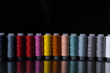 spools of colored thread stand in a row against a dark background with reflection. Copy space