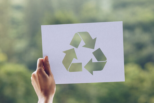 Cropped Hand Holding Paper With Recycling Symbol Cut Out Against Trees